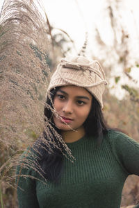 Thoughtful teenage girl wearing knit hat looking away on field by plants
