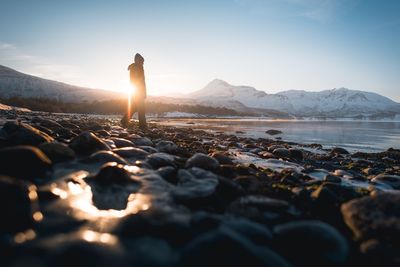 Surface level shot of silhouette person standing on rocks at shore during sunset