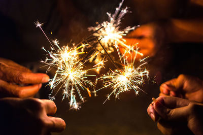 Cropped hands holding illuminated sparklers at night