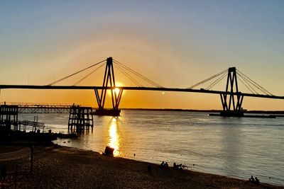 Silhouette bridge over sea against sky during sunset