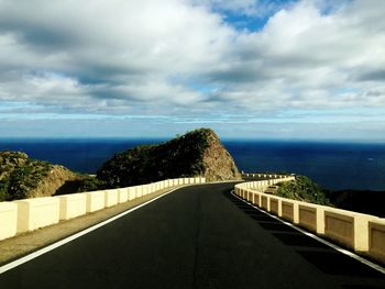 Road leading towards sea against cloudy sky