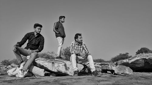 People sitting on rock against clear sky