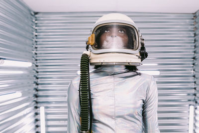 Serious professional african american female astronaut in helmet standing in modern light spaceship with silver walls before going on mission looking up