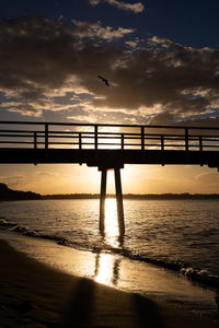 Silhouette bridge over sea against sky during sunset