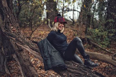 Smiling woman sitting on tree trunk at forest