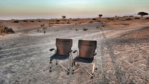 Chairs on sand at desert against clear sky