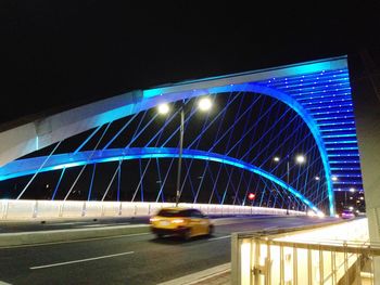 Illuminated bridge by road in city at night