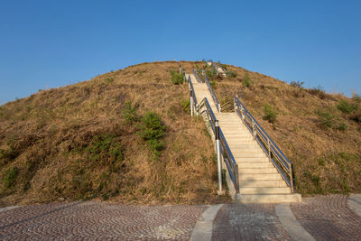 Footpath leading towards mountains against clear blue sky