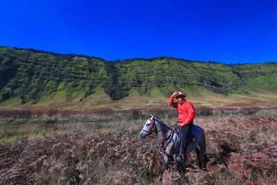 Man riding horse on field against sky during sunny day