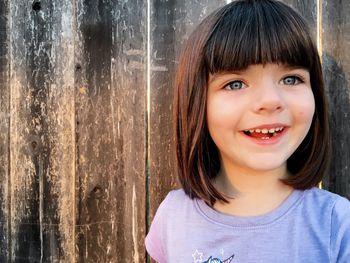 Close-up of happy girl against wooden fence