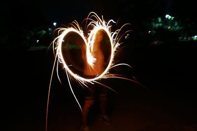 Young woman creating heart with sparkler at night