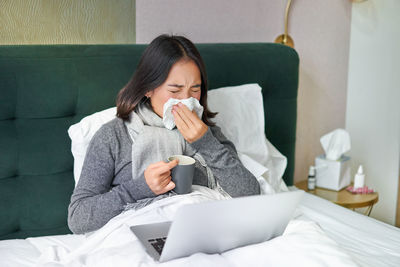 Young woman using mobile phone while lying on bed at home