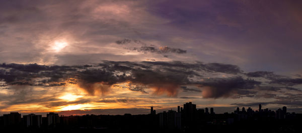 Silhouette cityscape against dramatic sky during sunset