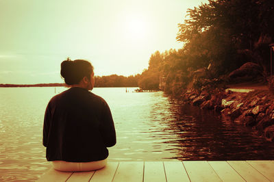 Rear view of man sitting by lake against sky