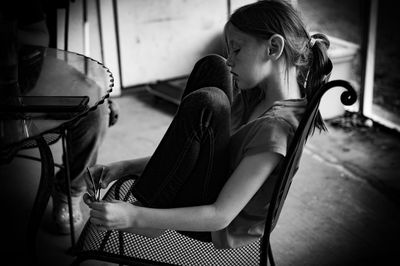 Side view of girl sitting on chair at home