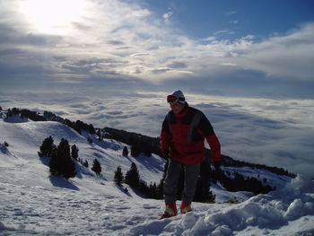 Man in warm clothing standing on snowcapped mountain against cloudy sky