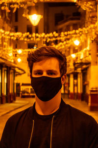 Portrait of young man against illuminated wall at night