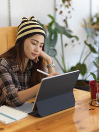 Young woman using digital tablet while sitting on table