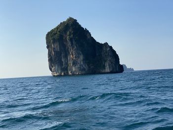 Rock formation in sea against clear blue sky