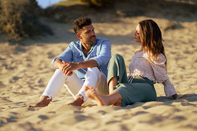 Couple talking while sitting on sand at beach