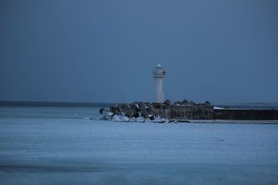 Lighthouse by sea and buildings against sky