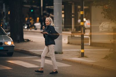 Senior woman looking away while walking on zebra crossing in city