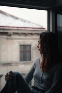 Woman looking away while sitting on window