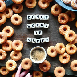 High angle view of hand holding coffee on table with doughnuts and words. donut worry be happy 