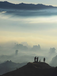 Silhouette people standing on mountain during foggy weather