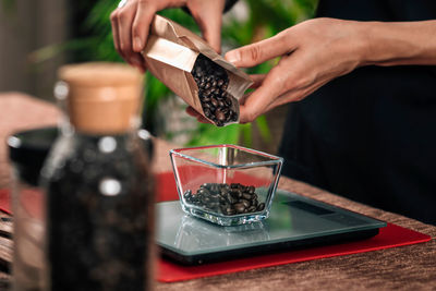 Weighing coffee grains on digital scale. hands of barista pouring roasted coffee grains on a scale