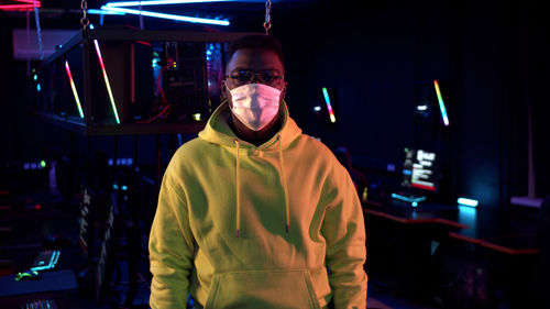 Portrait of young man wearing mask standing in internet cafe