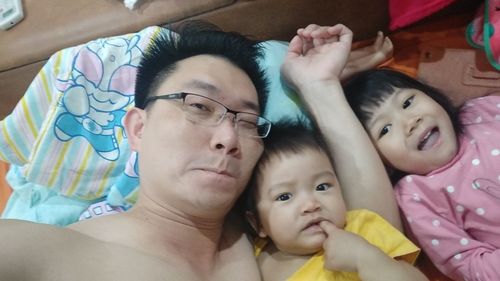 High angle portrait of shirtless father with children lying on bed at home