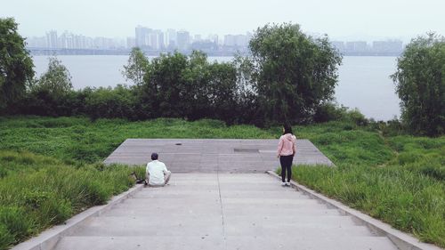 Rear view of people walking on retaining wall by river