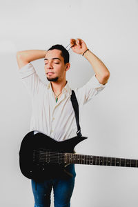 Young man with guitar standing against white background