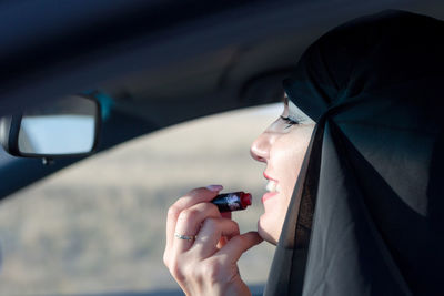Smiling woman applying lipstick while sitting at car