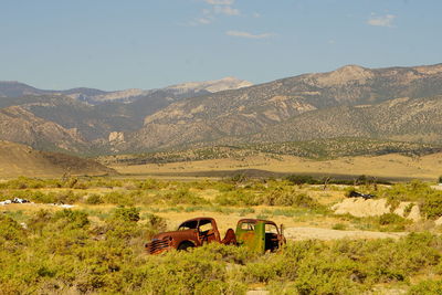 Abandoned car on field by mountains against sky