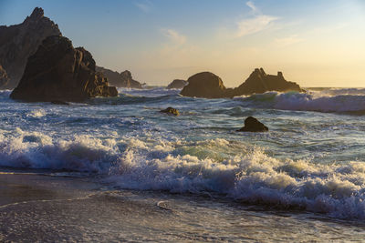 Scenic view of waves splashing at sea against sky