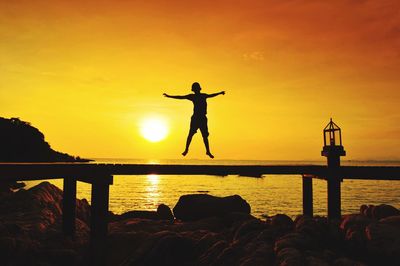 Silhouette of boy jumping on beach against orange sky