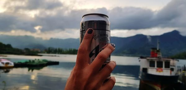 Midsection of person holding glass against lake