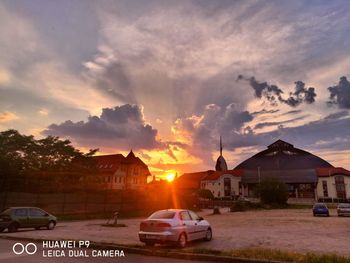 Cars on street by buildings against sky during sunset