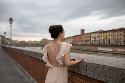 Rear view of woman standing by retaining wall against city