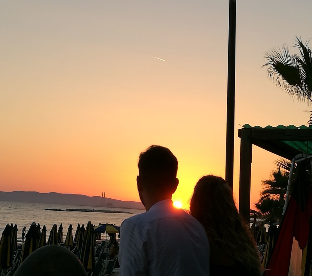 REAR VIEW OF COUPLE STANDING AT SEASIDE