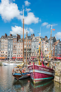 Boats moored at harbor against sky in city