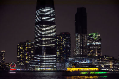 Illuminated buildings by river against sky in city at night