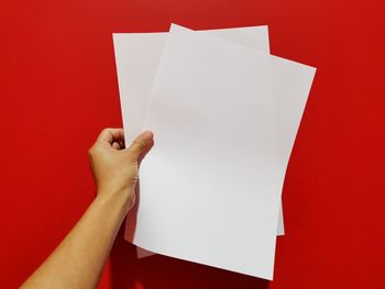 Close-up of hand holding paper against red background