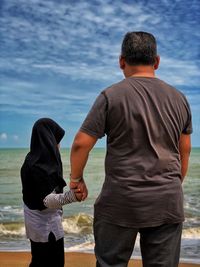 Father and daughter at beach against sky