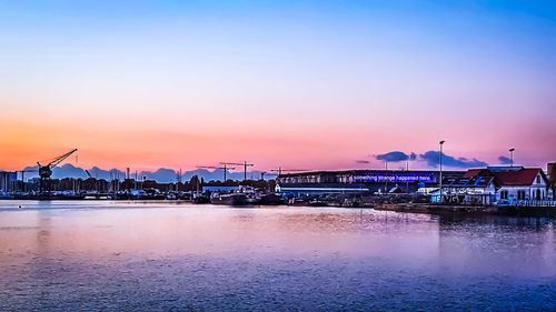 Illuminated buildings by sea against sky at sunset