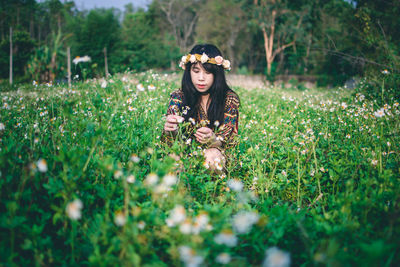 Woman wearing flowers while sitting on field 