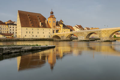 Arch bridge over river by buildings against sky