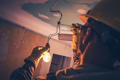 Rear view of electrician repairing light bulb at home